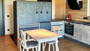 Moderni keittiö, jossa on puulattia, ruokailutila pöydän ja tuolien kera sekä sisäänrakennettu uuni.