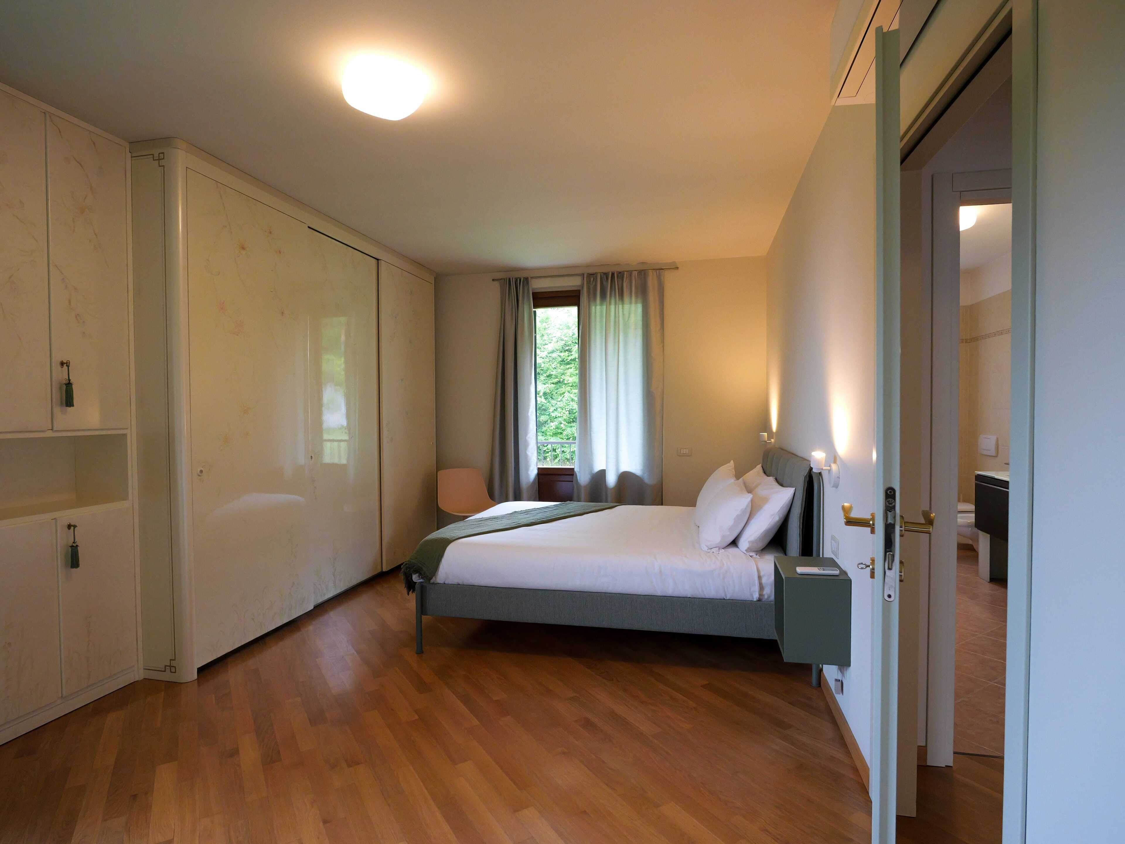 A bedroom with a bed, a nightstand, a wardrobe, and a bathroom visible through an open door.