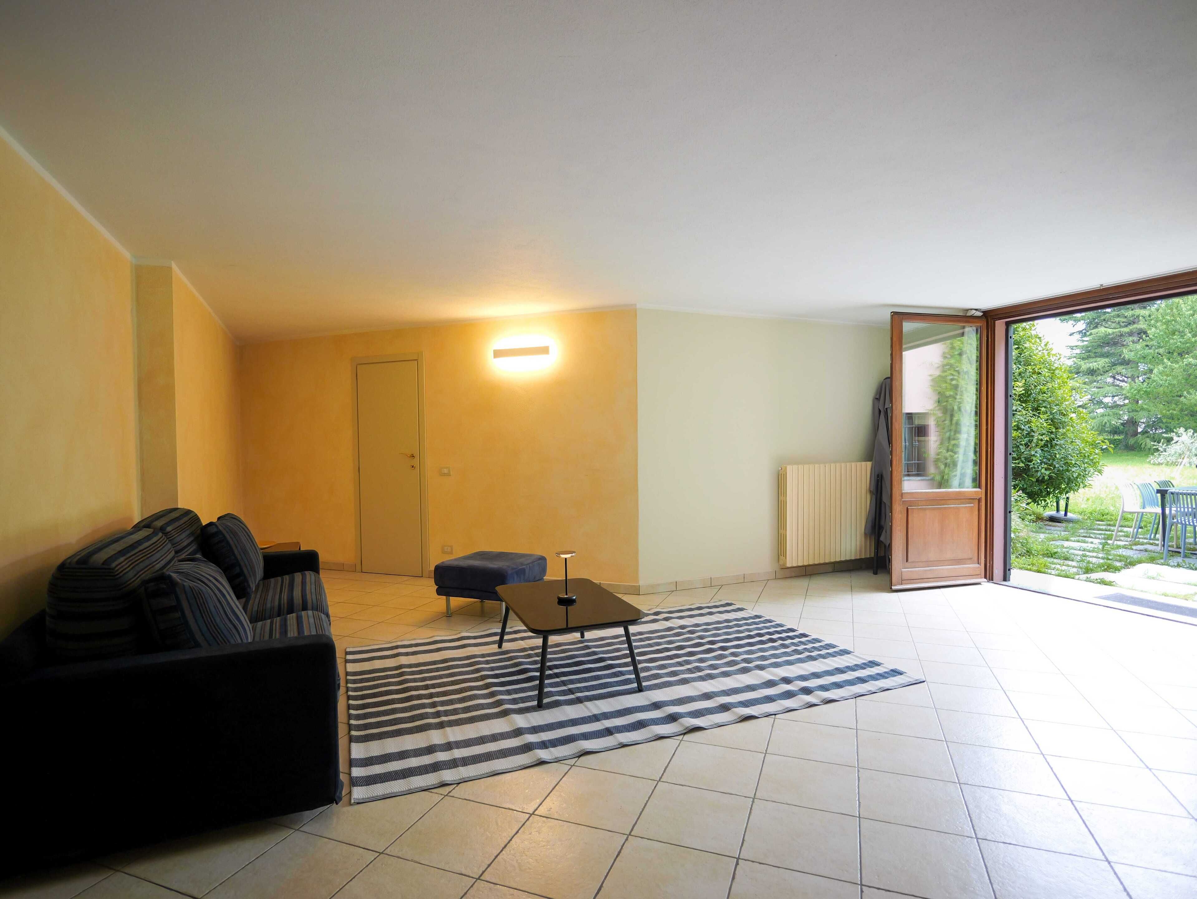 A living room with a sofa, a small table, a striped rug, and a sliding glass door leading to a garden.