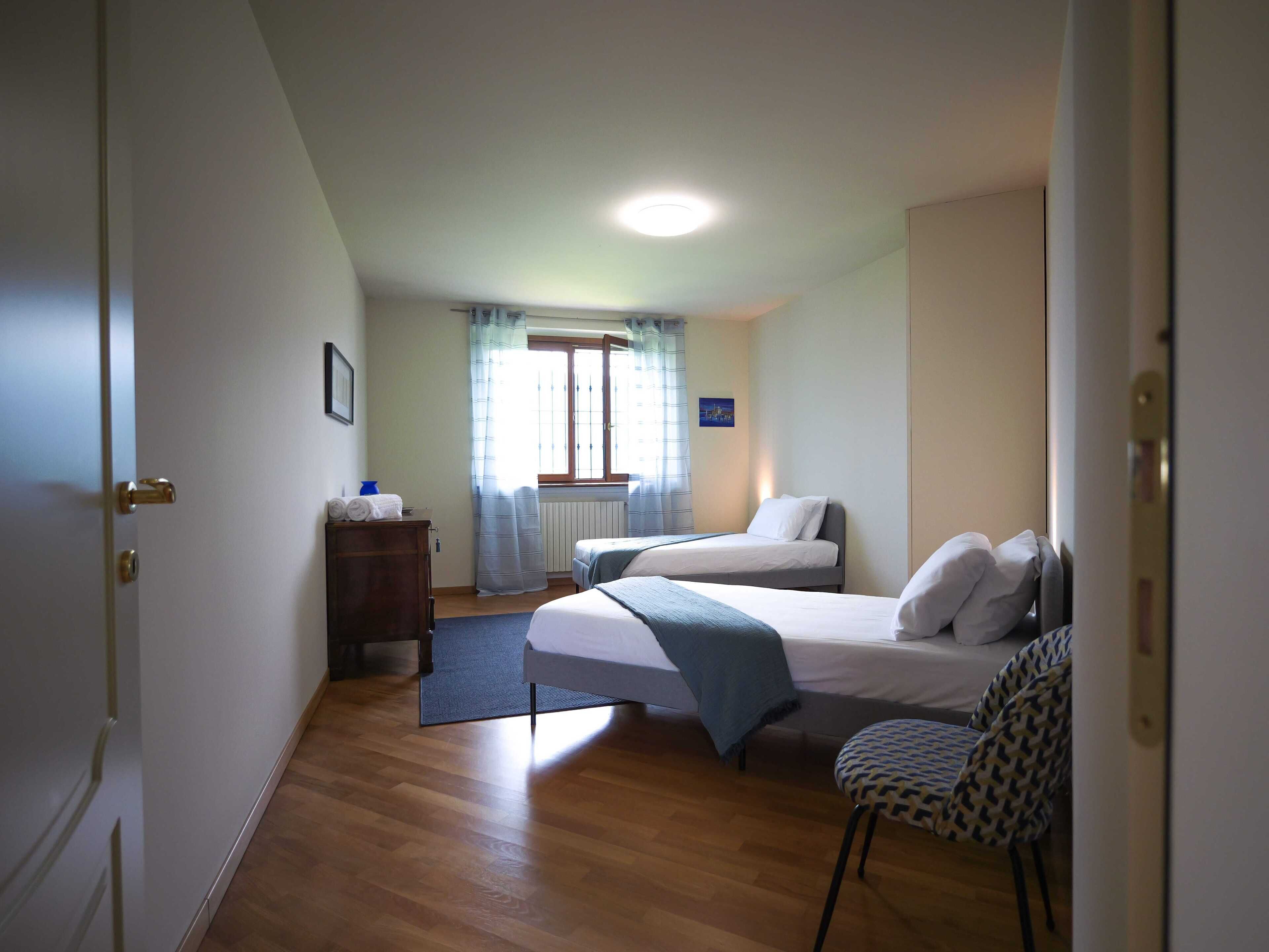 A hotel room with two beds, a chair, a dresser, and a window with curtains.