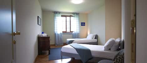 A hotel room with two beds, a chair, a dresser, and a window with curtains.
