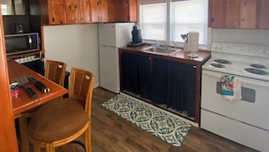 Une cuisine compacte dotée de meubles en bois, d’un réfrigérateur, d’un four à micro-ondes, d’une cuisinière et d’un coin repas avec une table et des chaises.