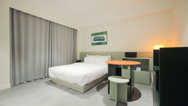 Een hotelkamer met een bed, een klein tafeltje, een nachtkastje en een aan de muur bevestigde televisie.