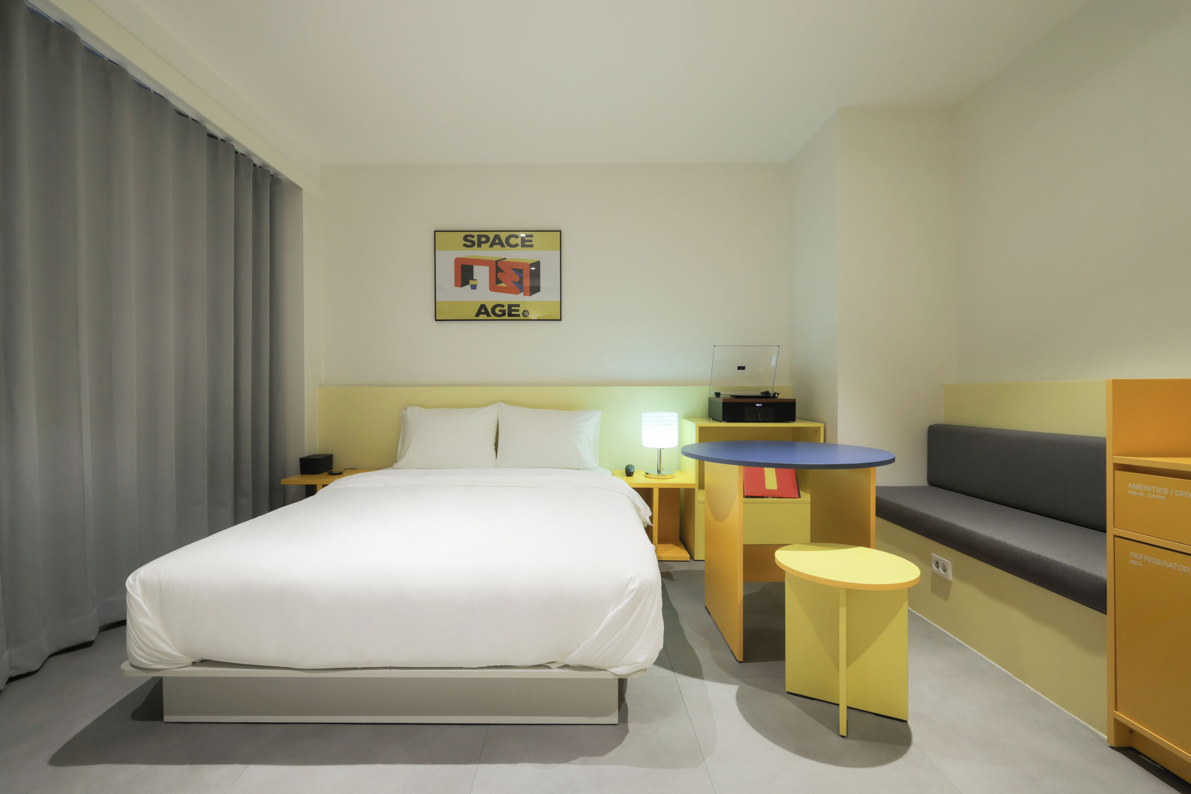 A hotel room with a bed, a desk, a chair, a sofa, and a wall-mounted sign.
