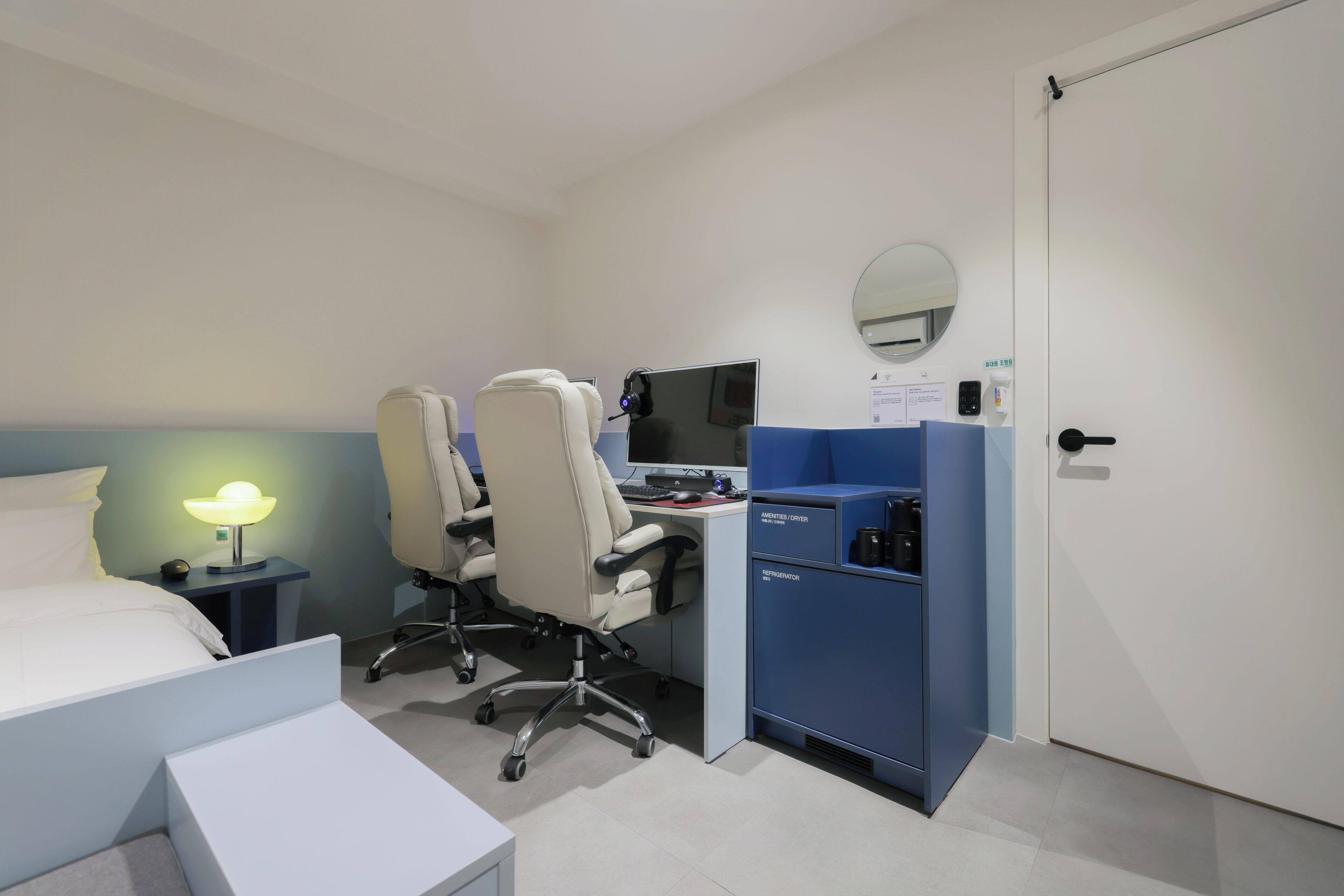 A hotel room with a bed, desk, computer, chair, and a blue storage unit.