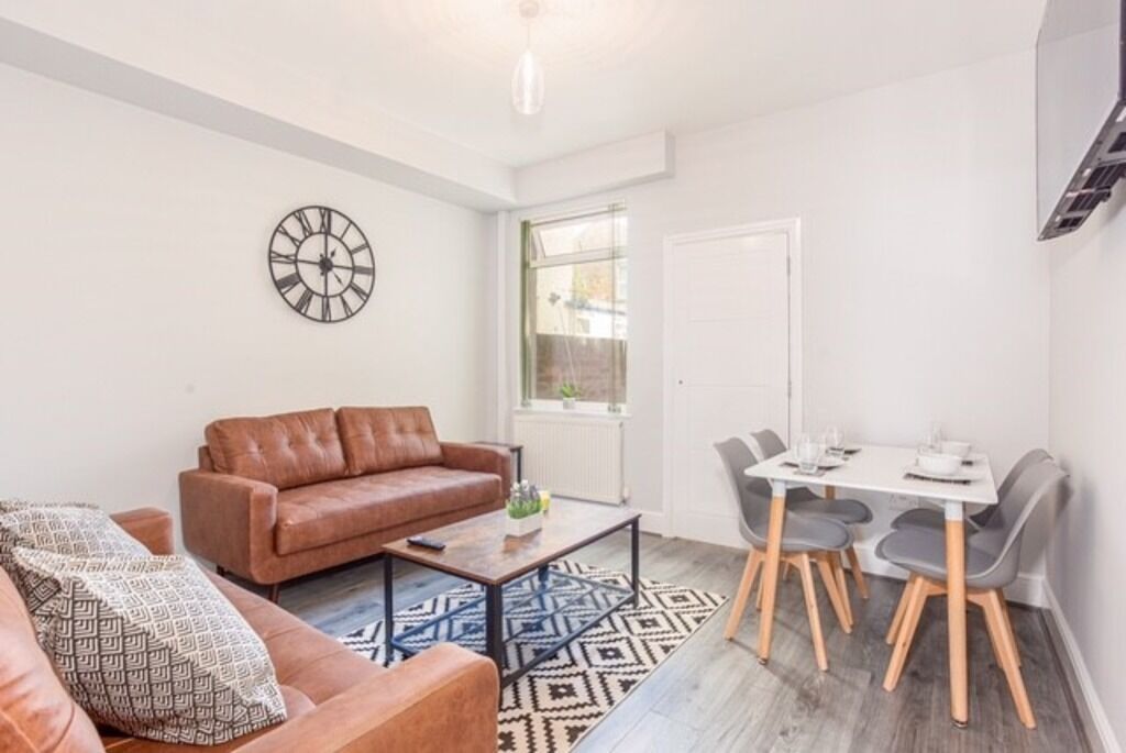 A living room with a brown leather sofa, a coffee table, and a dining area with a white table and grey chairs.
