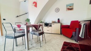 A dining area with a high arched ceiling, a dining table with chairs, a red sofa, a clock, and a painting on the wall. - A Pochi Kilometri dal Mare di Sabaudia e dal Parco del Circeo, Piscina Esterna (Zona Industriale Borgo San Donato)