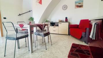 Ein Essbereich mit hoher, gewölbter Decke, einem Esstisch mit Stühlen, einem roten Sofa, einer Uhr und einem Gemälde an der Wand.