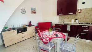 A compact kitchen with a dining area, featuring a red table and chairs, a clock, and a small plant on the counter. - A Pochi Kilometri dal Mare di Sabaudia e dal Parco del Circeo, Piscina Esterna (Zona Industriale Borgo San Donato)