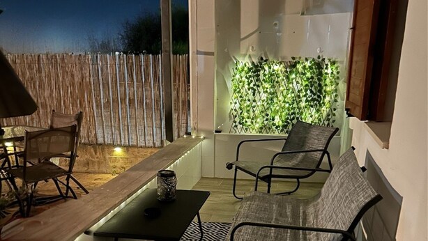 An outdoor patio with a table and two chairs, a wooden fence, and a wall with green foliage. - A Pochi Kilometri dal Mare di Sabaudia e dal Parco del Circeo, Piscina Esterna (Zona Industriale Borgo San Donato)
