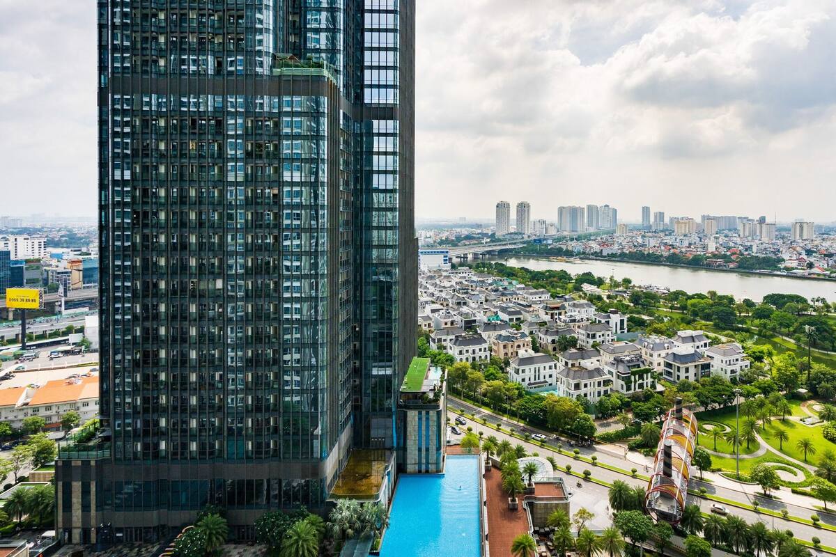 Un edificio moderno de gran altura con fachada de vidrio, piscina en la azotea y vistas al río y al paisaje urbano.