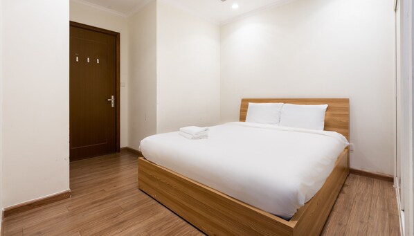 A neatly made bed with white linens and a wooden headboard in a clean, white-walled room with a wooden floor. - Vinhomes Central Park Luxury - Leminbo (Ho Chi Minh City)