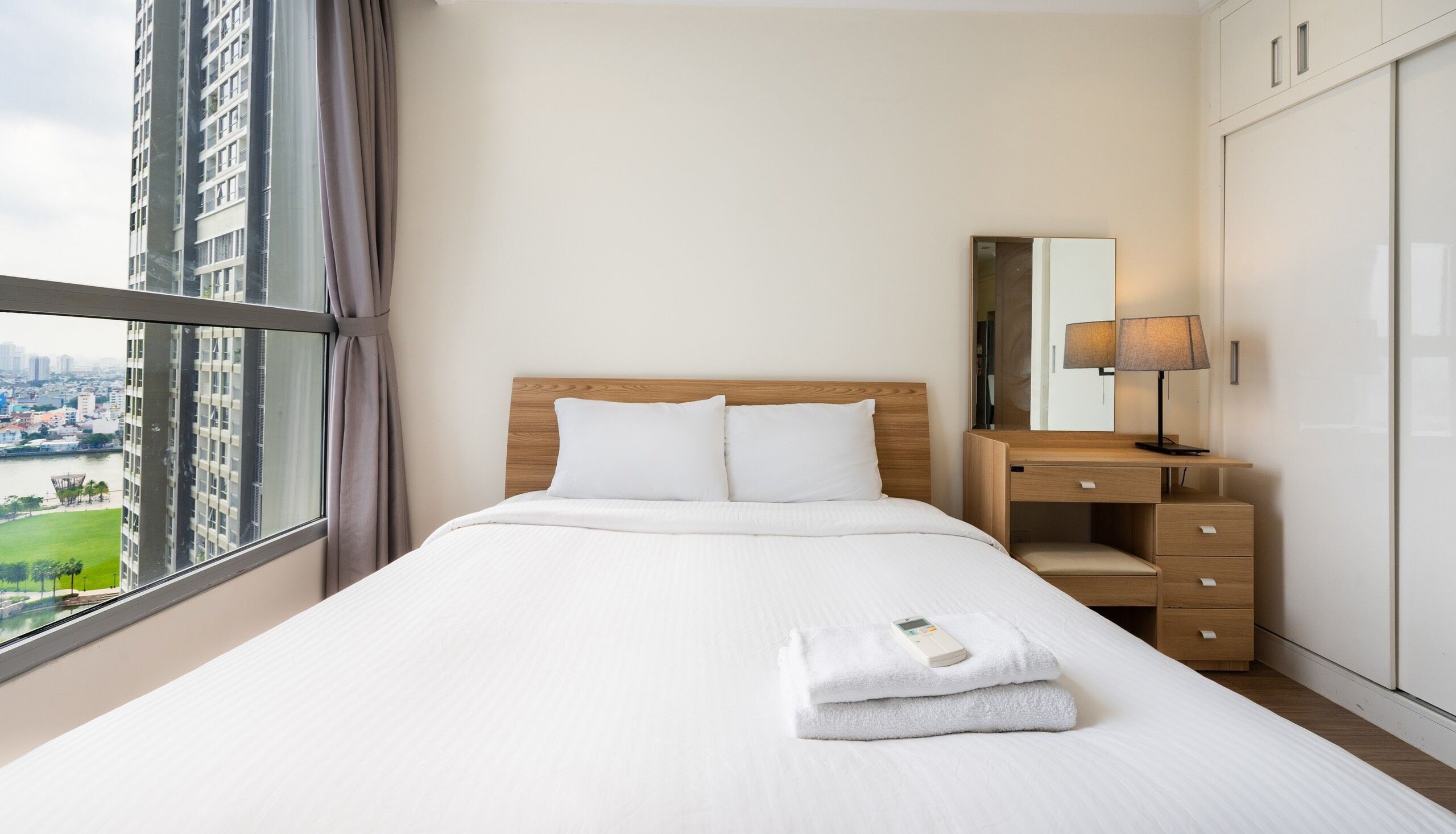 Een hotelkamer met een groot bed, een houten nachtkastje, een bureau en uitzicht op een stadsbeeld door een raam.