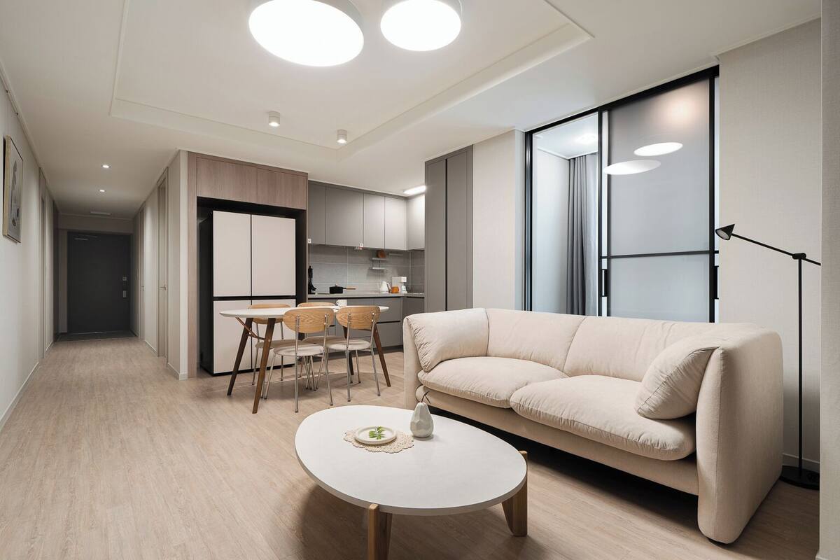 A modern living room with a beige sofa, a round coffee table, and a dining area with a table and chairs.