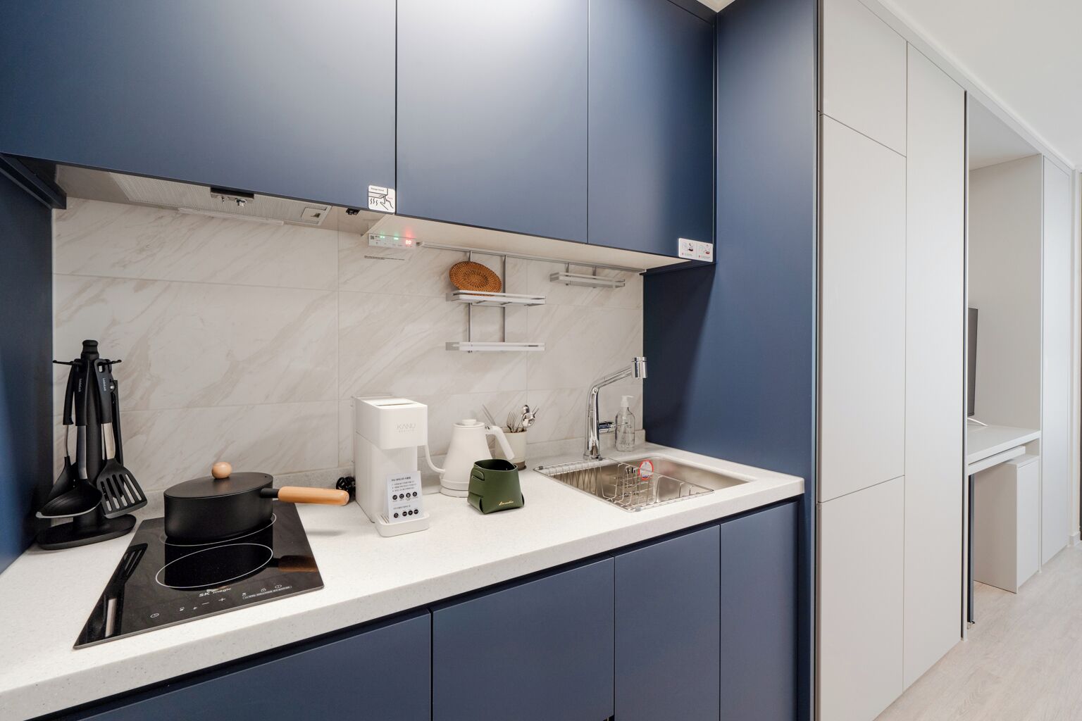 Una cocina moderna con encimera blanca, horno empotrado, cafetera y pileta.