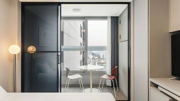 Habitación de hotel moderna con cama, una mesita redonda, dos sillas, televisor y ventana grande con vistas a la ciudad.