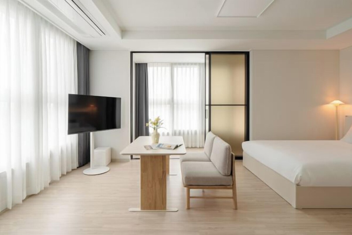 A modern hotel room with a flat-screen TV, a sofa, a bed, a small table, and a lamp.