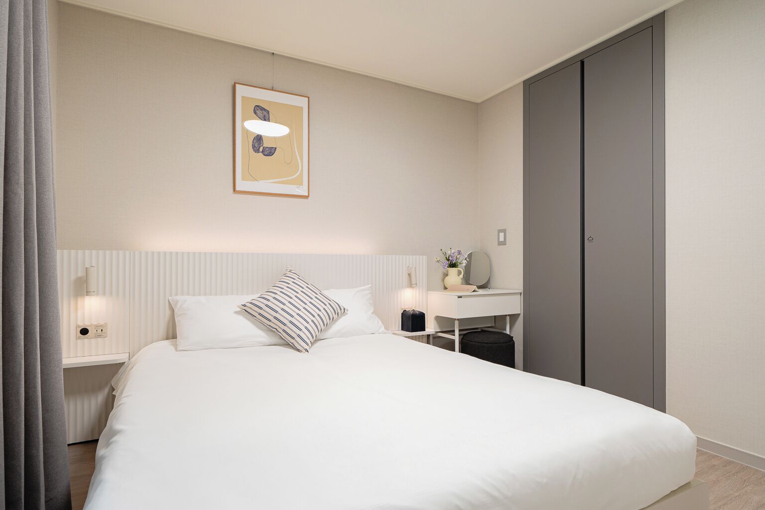 A modern hotel room with a large bed, bedside tables, a desk, and a wardrobe.