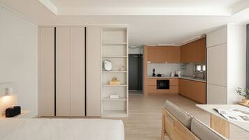 A modern, minimalist hotel room with a bed, bedside table, and a view of the kitchen area.