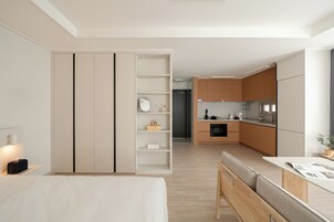 A modern, minimalist hotel room with a bed, bedside table, and a view of the kitchen area.