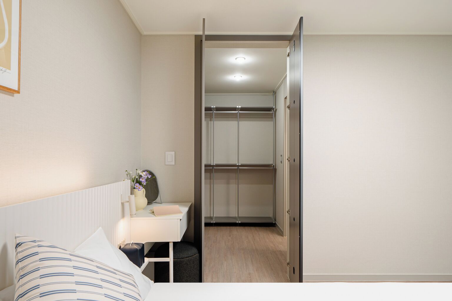A bedroom with a bed, bedside table, and a desk with a chair. There is a wardrobe with a mirror and a door leading to a bathroom.