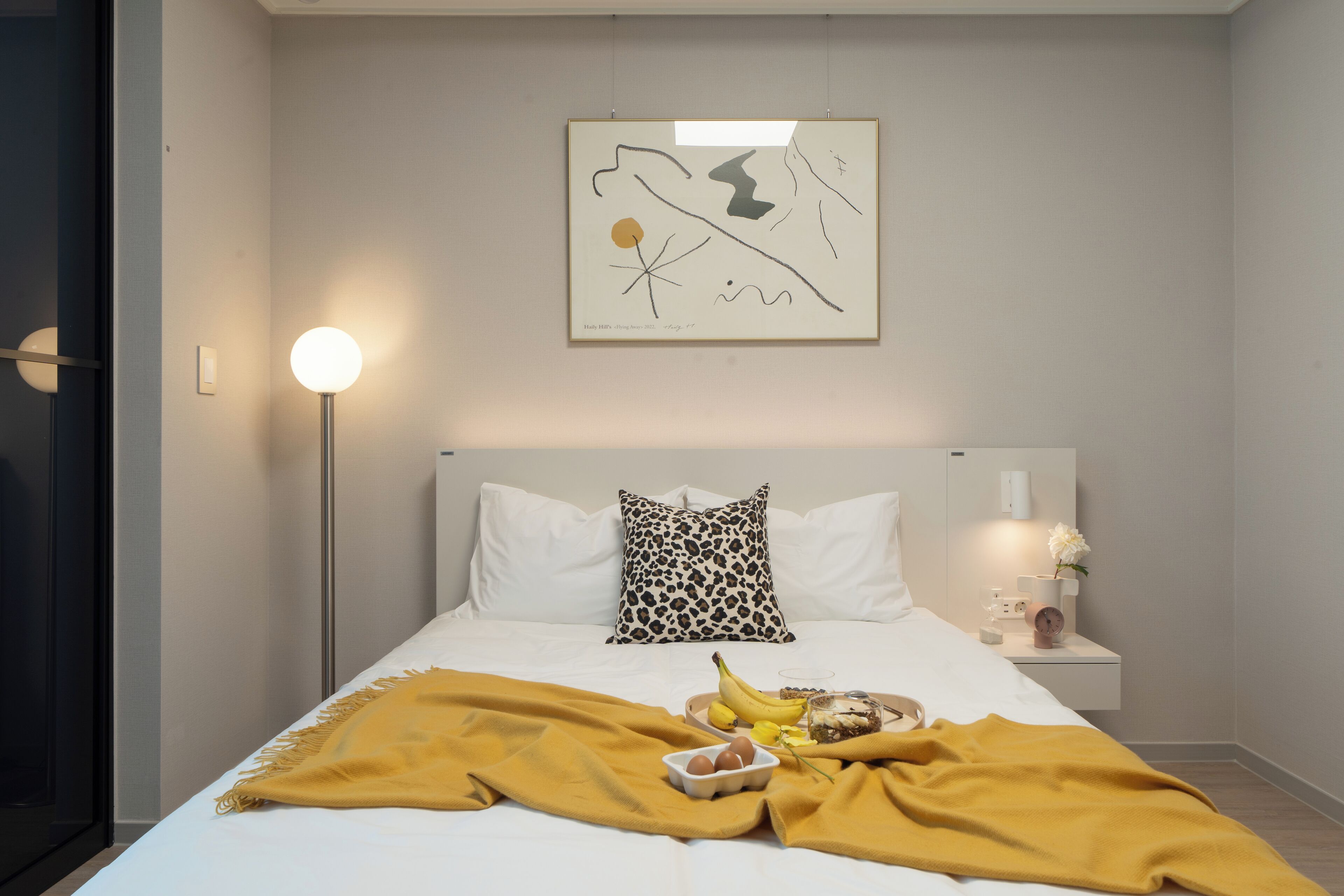 A modern bedroom with a bed, a bedside table with a lamp, a wall art piece, and a yellow throw blanket.