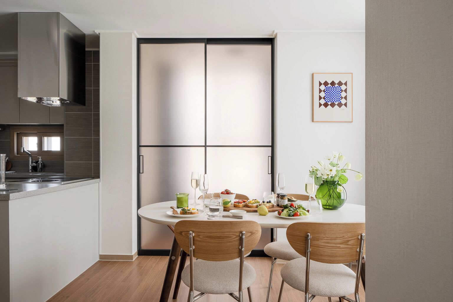 A modern kitchen with a dining area, featuring a large window, a stainless steel range hood, and a dining table set with chairs.