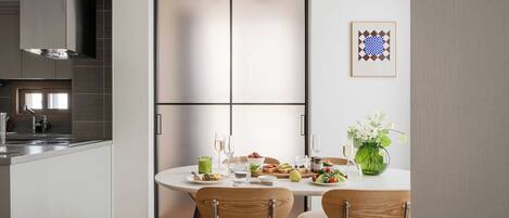 A modern kitchen with a dining area, featuring a large window, a stainless steel range hood, and a dining table set with chairs.