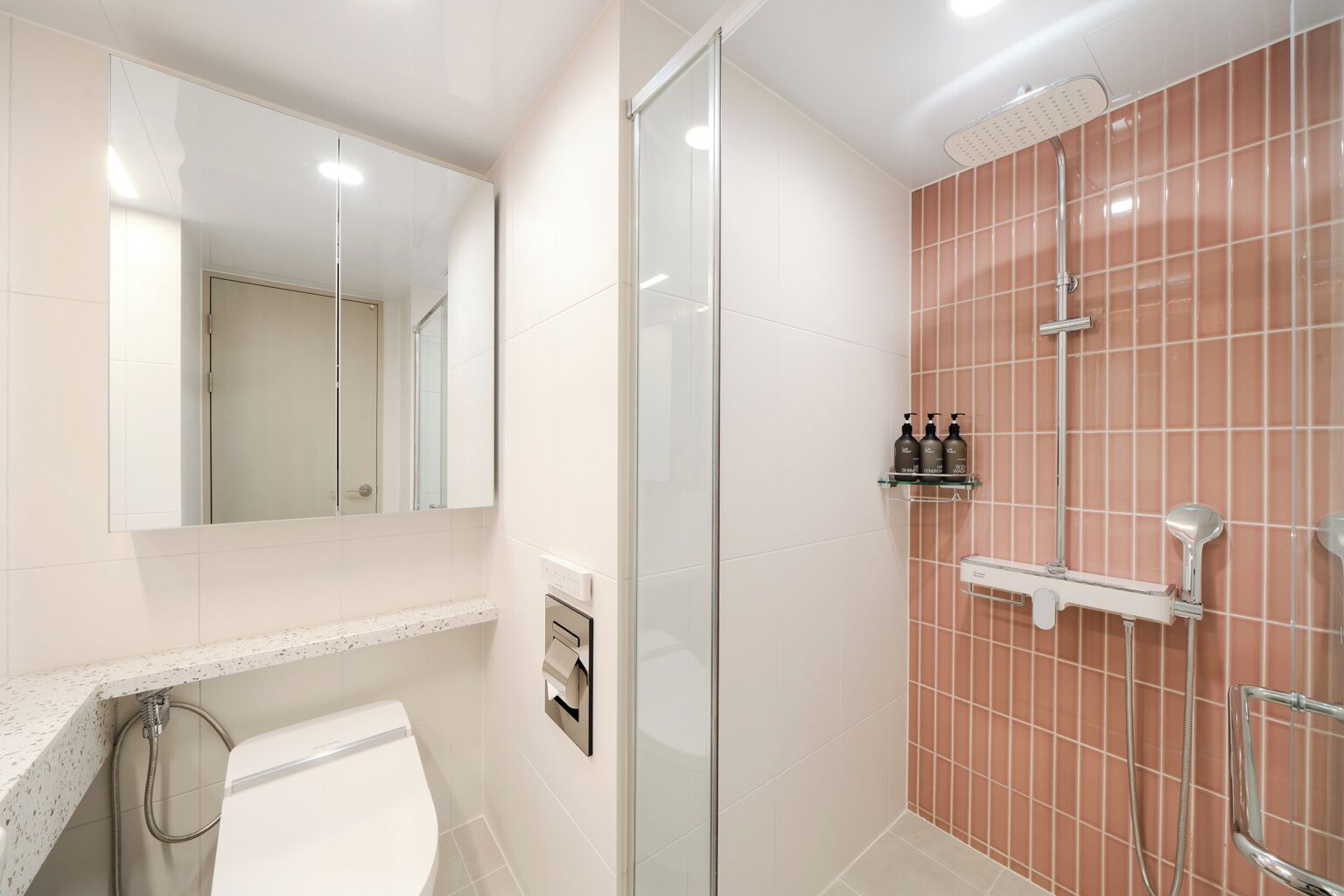 Een moderne badkamer met een douchecabine van glas, een wit wastafel en een badkamermeubel met een spiegel.