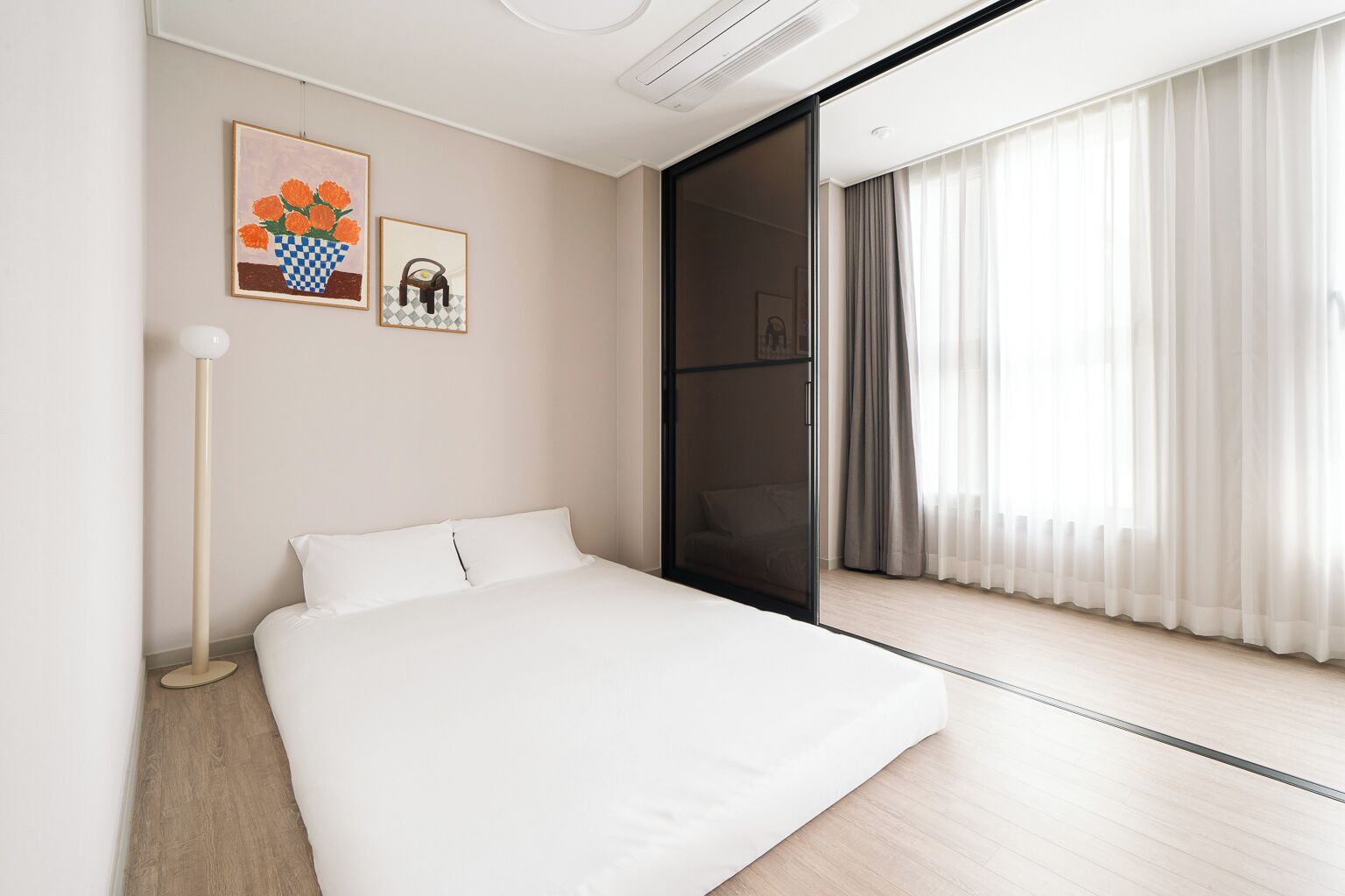A modern hotel room with a large bed, a floor lamp, and a sliding glass door leading to a balcony with curtains.