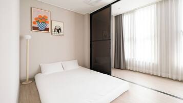 A modern hotel room with a large bed, a floor lamp, and a sliding glass door leading to a balcony with curtains.