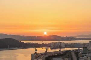 Une vue d’une ville au coucher du soleil, avec une rivière, une zone industrielle et des immeubles de grande hauteur.