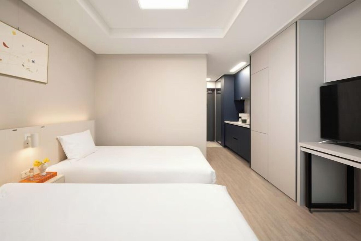 Une chambre d’hôtel moderne équipée de deux lits, d’une télévision et d’un petit bureau.