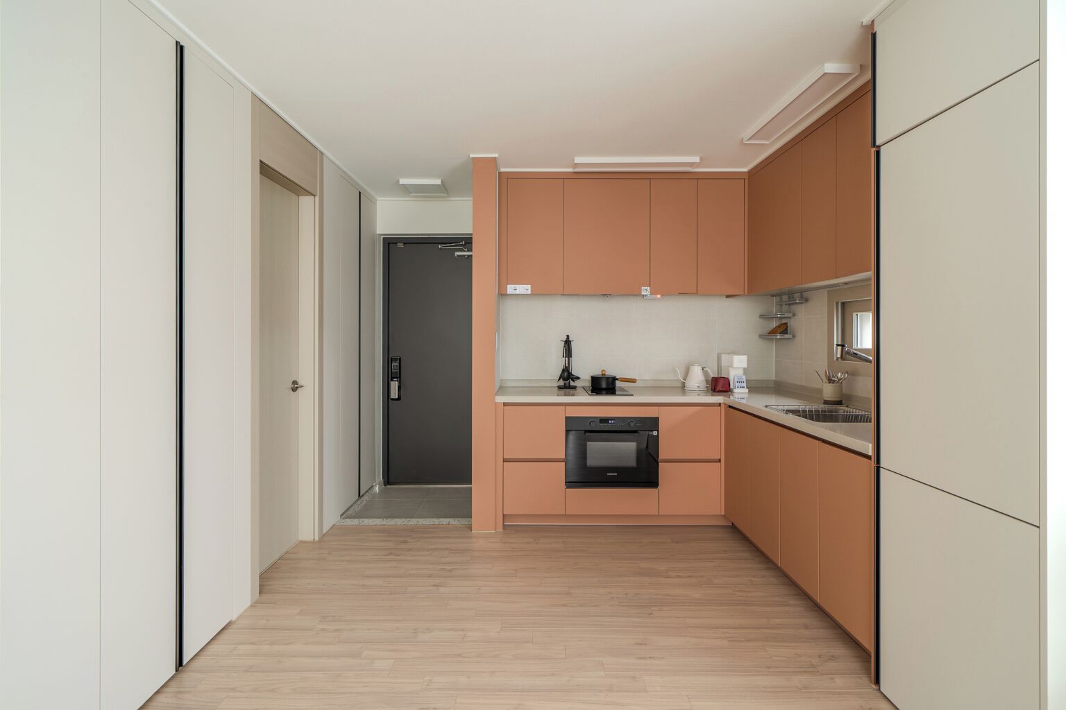 A modern kitchen with wooden cabinets, a built-in oven, and a countertop with a kettle and coffee maker.