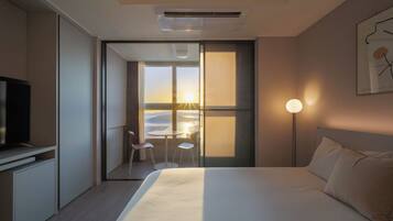 Une chambre d’hôtel avec un lit, une télévision, un bureau avec des chaises et une vue sur le coucher de soleil, visible à travers de grandes fenêtres.