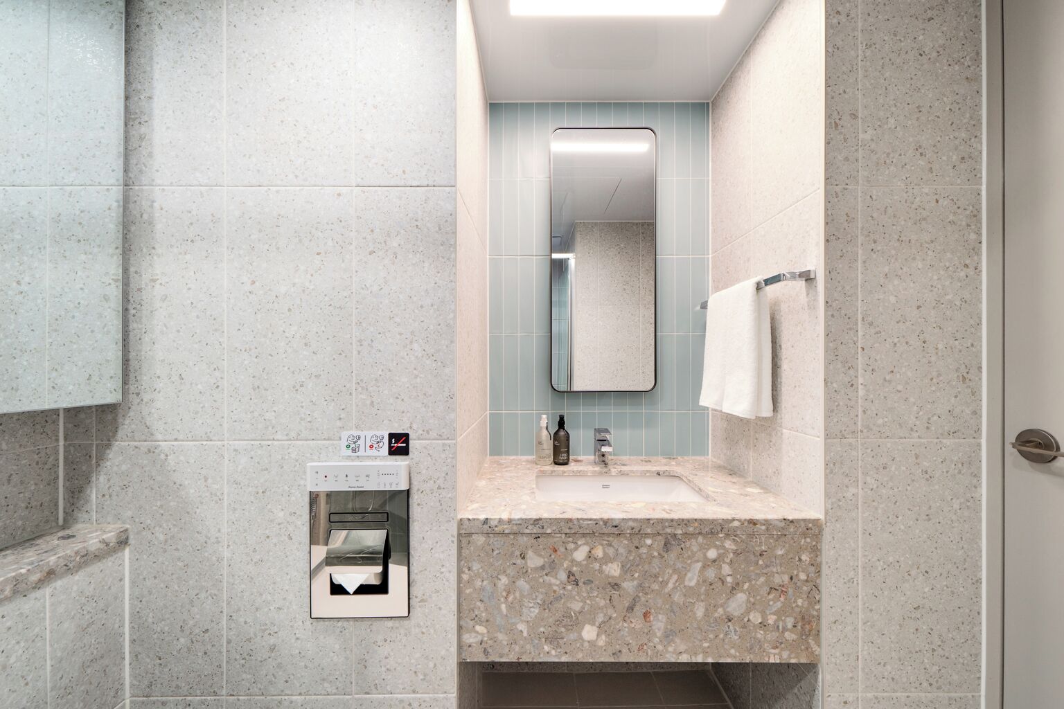 A modern bathroom with a marble sink, a mirror, and a towel rack.