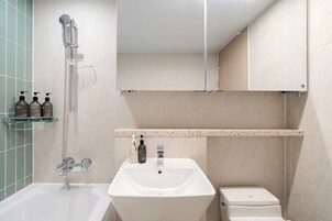 A modern bathroom with a bathtub, a sink, and a toilet. There are three bottles of shampoo and conditioner on a shelf.