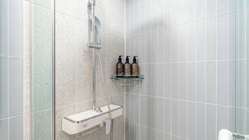 A shower area with a handheld showerhead, a wall-mounted faucet, and a glass shelf with three bottles of shampoo and conditioner.