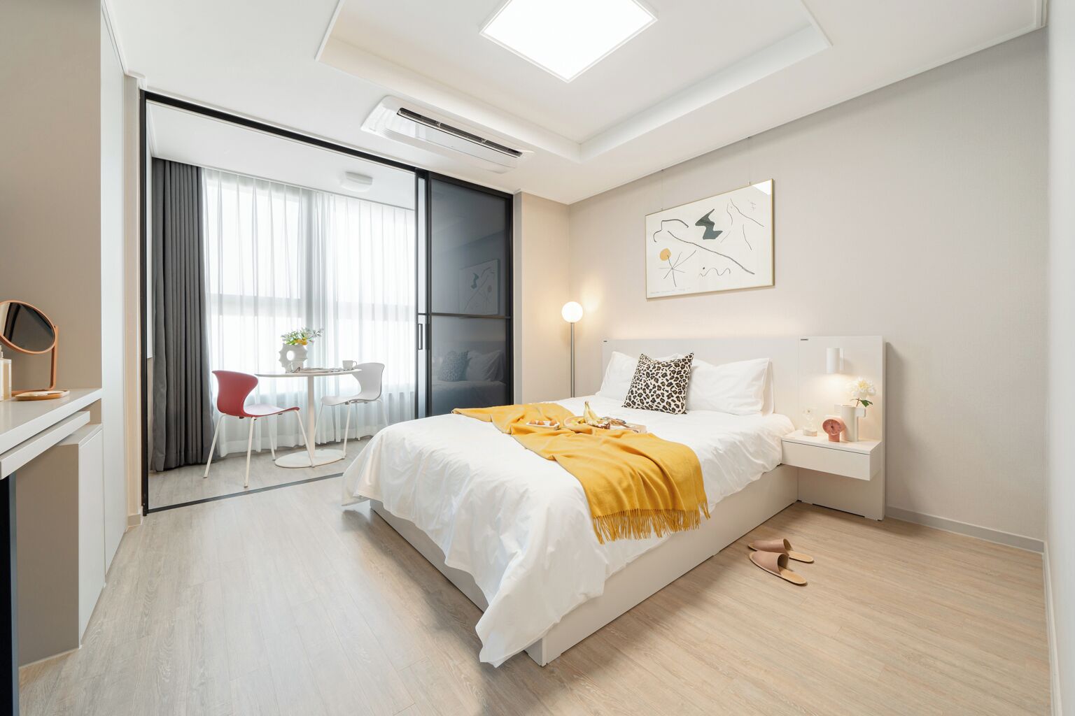 Una habitación de hotel moderna con una cama, mesita de noche y un escritorio con una silla. Hay una puerta corredera que da a un balcón con mesa y sillas.