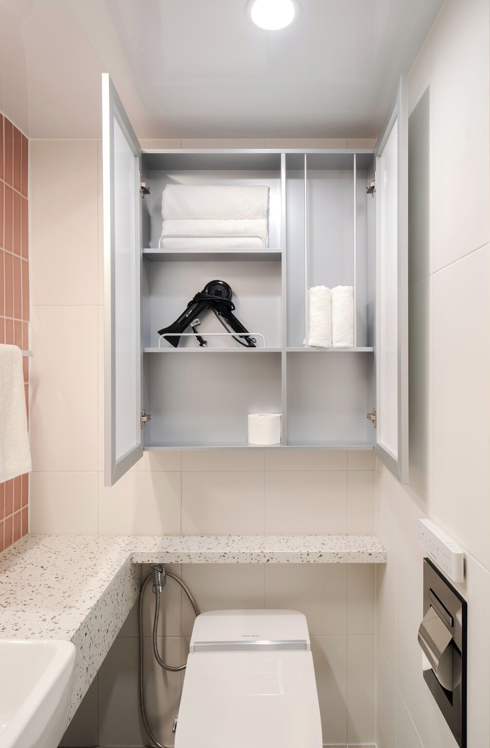 Baño con armario empotrado que contiene toallas, un secador de pelo y papel higiénico.
