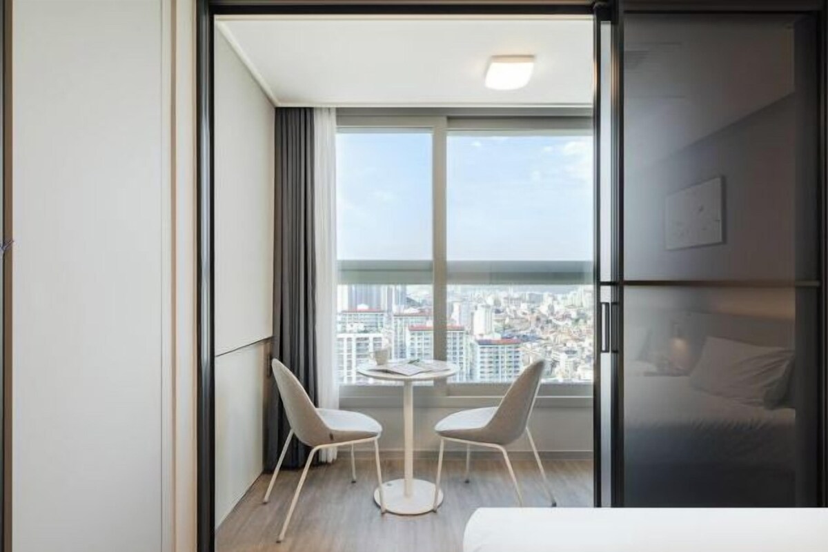 A modern hotel room with a balcony, a small table with two chairs, and a bed.