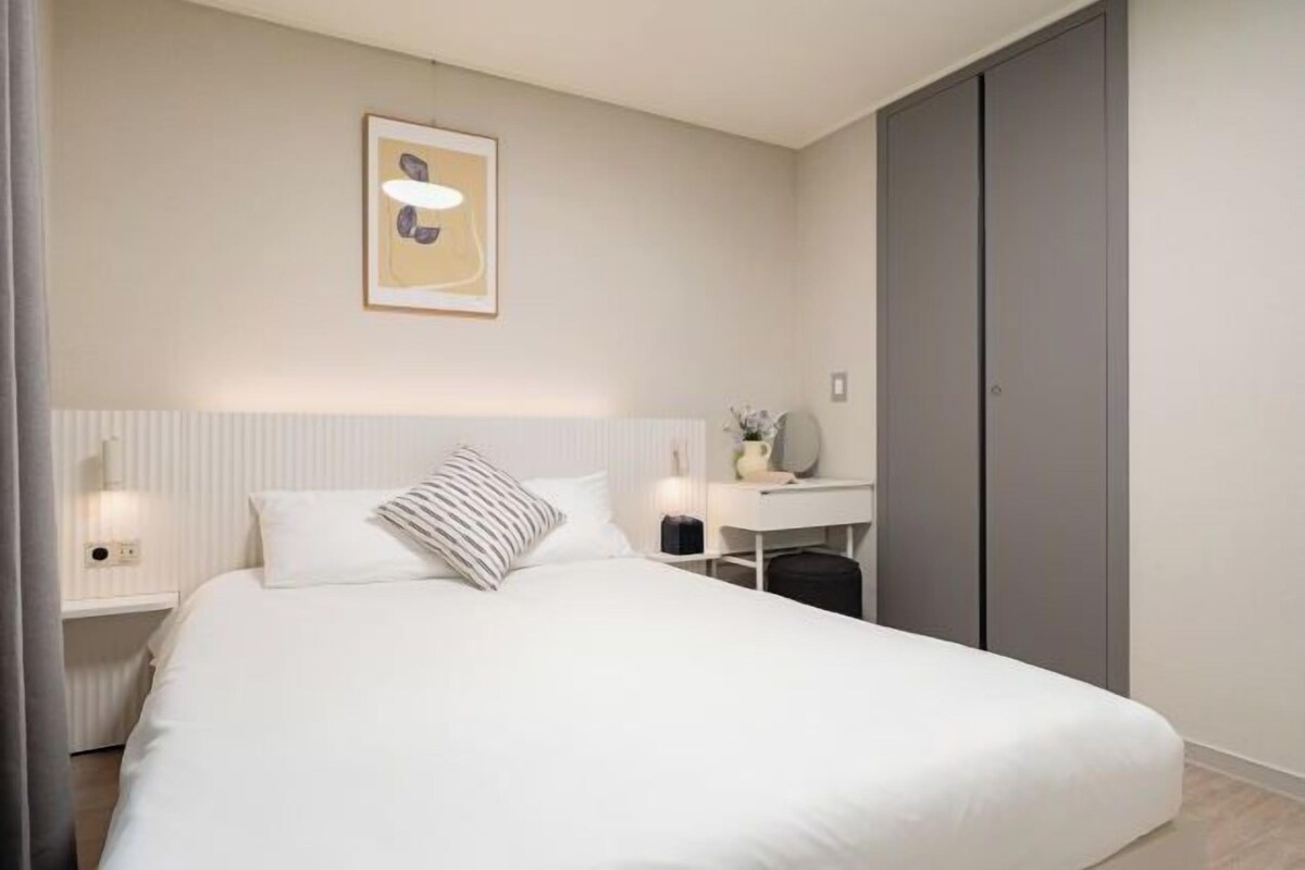 A bedroom with a bed, a bedside table, a desk, and a wardrobe.