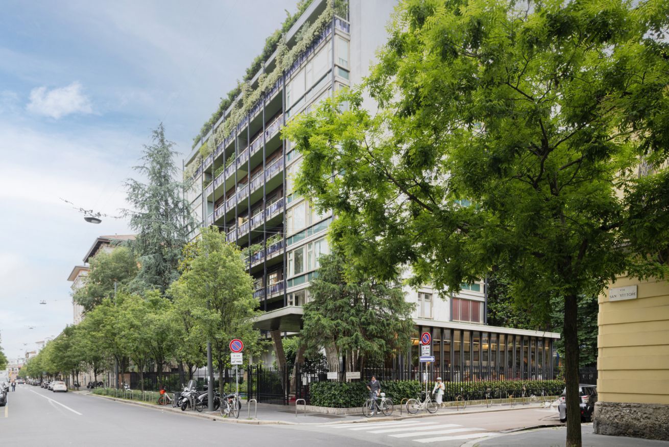 A modern urban street with a multi-story building featuring balconies with greenery.