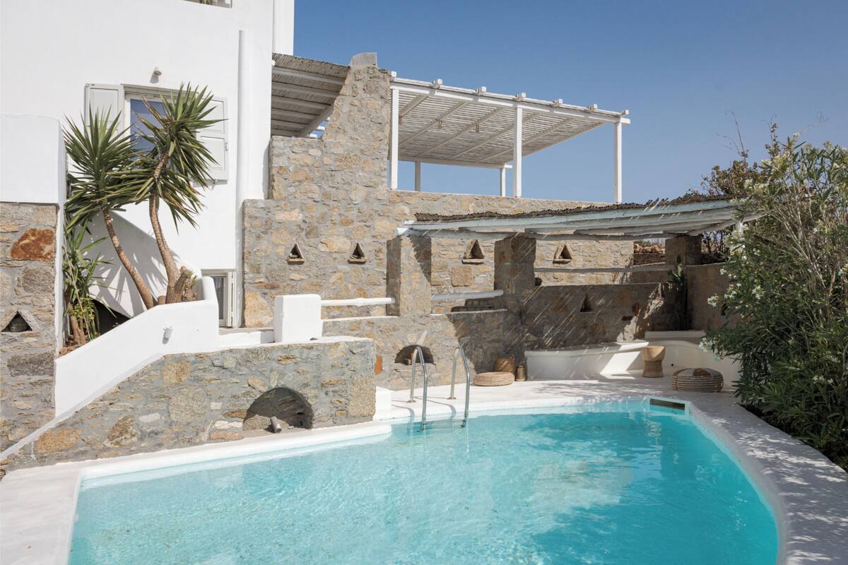 Ein Poolbereich mit Steinmauern, einer Pergola und einer Palme.