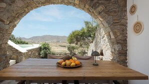 Un arc en pierre mène à une table en bois sur laquelle se trouvent un panier de fruits et une lampe, le tout offrant une vue sur un paysage pittoresque.