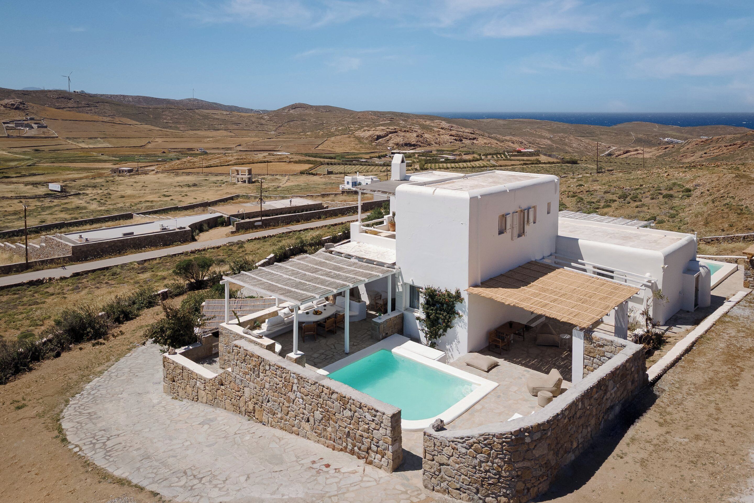 A modern villa with a swimming pool, a covered outdoor seating area, and a view of the surrounding landscape.