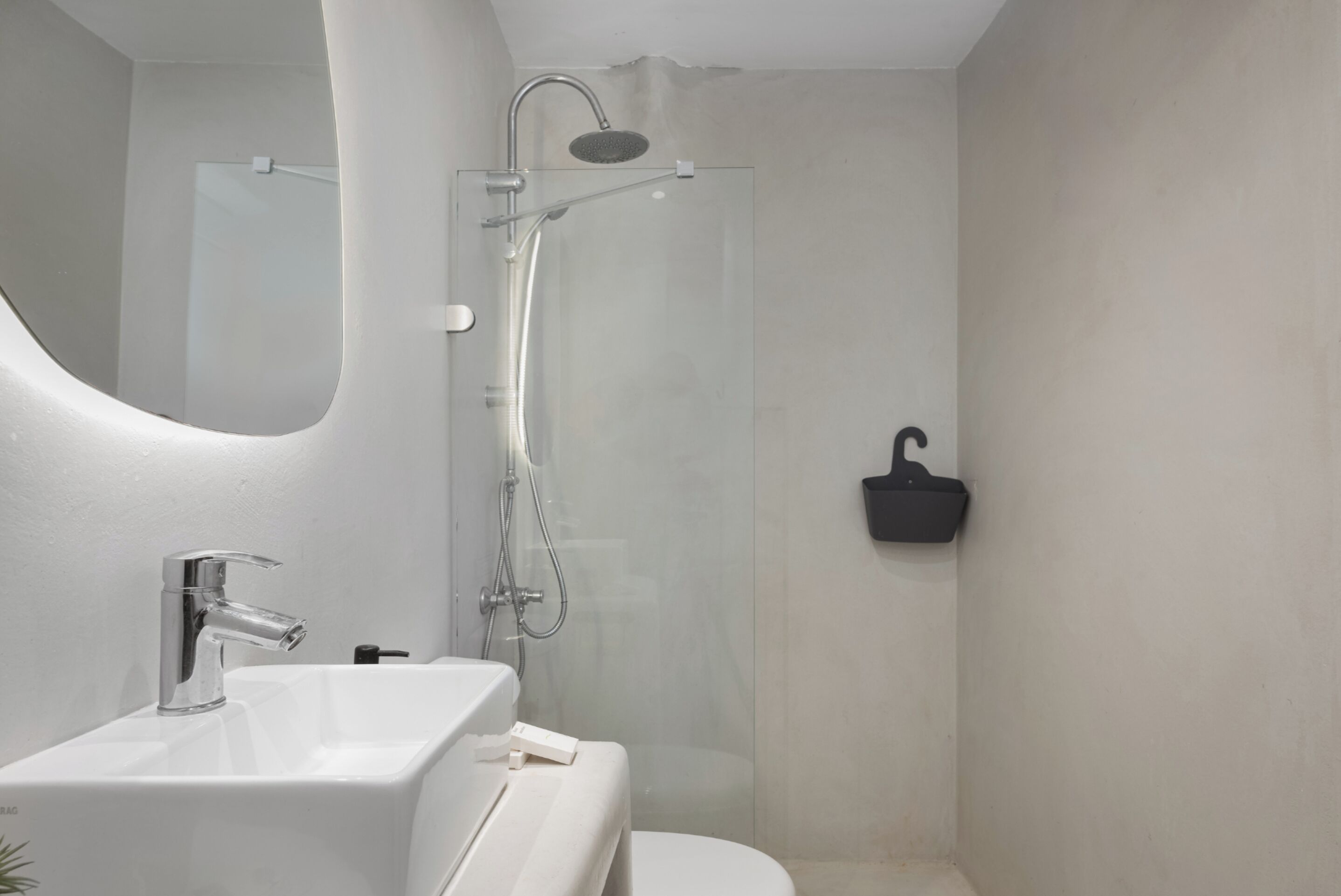 A modern bathroom with a white sink, a shower, and a black soap dish.