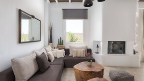 Un salon moderne avec un canapé d’angle, une table basse ronde en bois, une cheminée et une grande fenêtre offrant une belle vue.