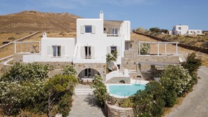 Une villa blanche avec une piscine, entourée de verdure et située au pied d’une colline.