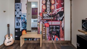 A room with a guitar, a wooden bench, and a wall decorated with various posters and signs, including one for a boot country and a whiskey bar. - Double the Comfort | Travel Together (Prescott)